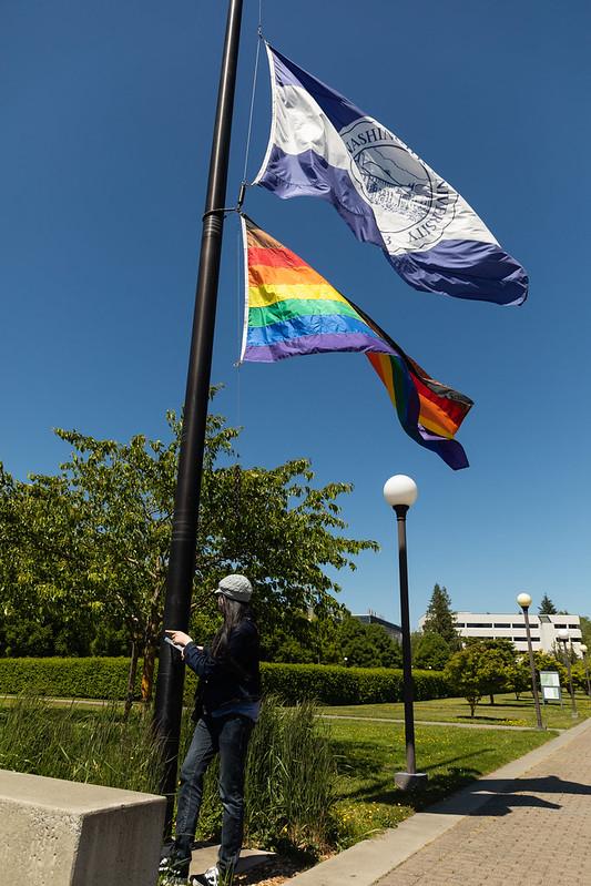 student raising a pride flag on WWU flag plaza